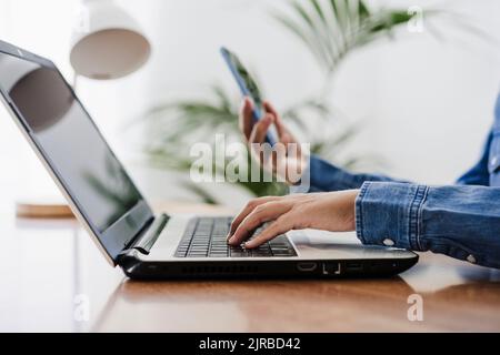 Freelancer using laptop holding smart phone at home office Stock Photo