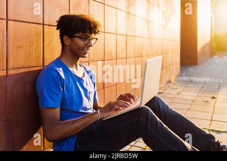Smiling man using laptop for studying sitting by wall Stock Photo
