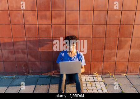 Young man using laptop for studying sitting leaning on wall Stock Photo
