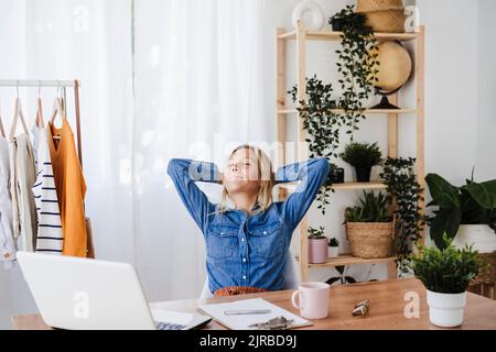 Smiling businesswoman with hands behind head resting at home office Stock Photo