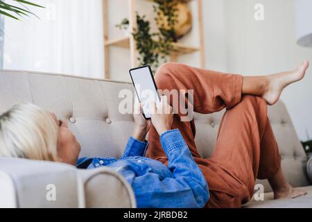 Woman using smart phone on sofa at home Stock Photo