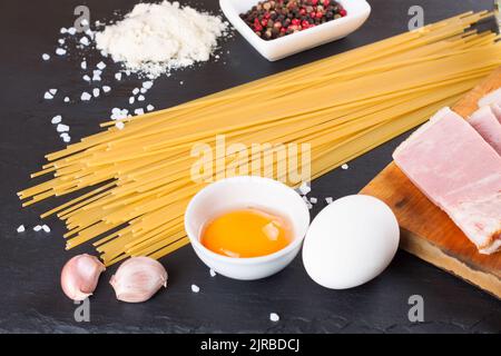 Ingredients for Pasta Carbonara on dark slate background. Spaghetti, ham, egg yolk, parmesan cheese, garlic and spices. Traditional italian cuisine Stock Photo