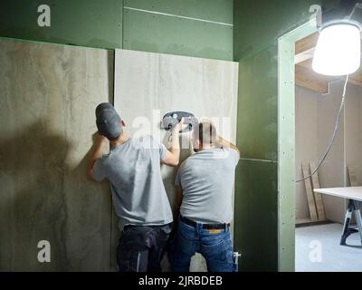 Tilers installing tiles on wall with vacuum cup at construction site Stock Photo