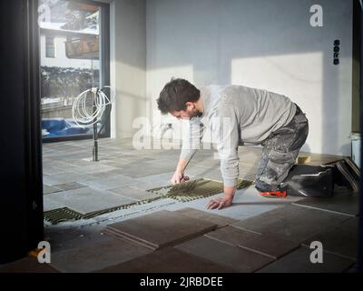 Young tiler applying adhesive on floor at construction site Stock Photo