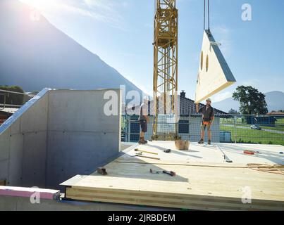 Colleagues working on rooftop with help of crane at construction site Stock Photo