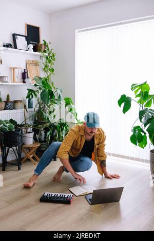 Man with laptop and piano on floor in living room at home Stock Photo