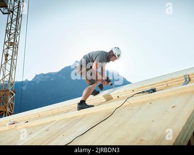 Carpenter working with drill on roof at construction site Stock Photo