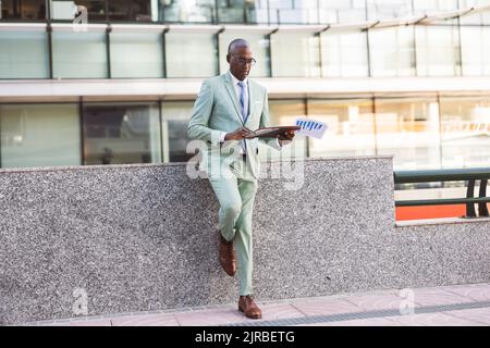 Mature businessman with documents leaning on wall Stock Photo