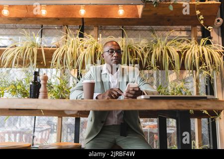Mature businessman using smart phone sitting at table in cafe Stock Photo