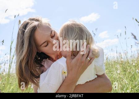Mother kissing daughter on sunny day at field Stock Photo