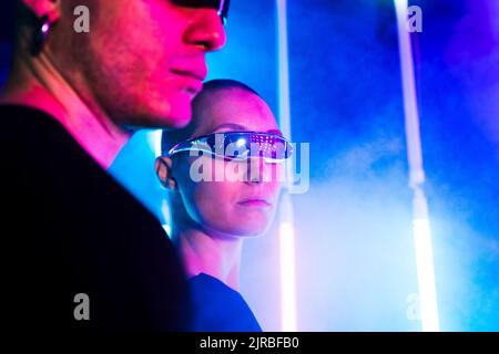Young woman wearing futuristic glasses by man near illuminated background Stock Photo