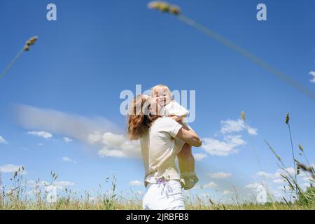Mother kissing happy daughter in front of sky Stock Photo