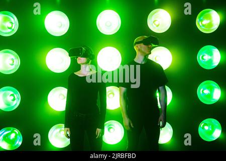 Couple wearing VR glasses standing in front of green neon lights Stock Photo