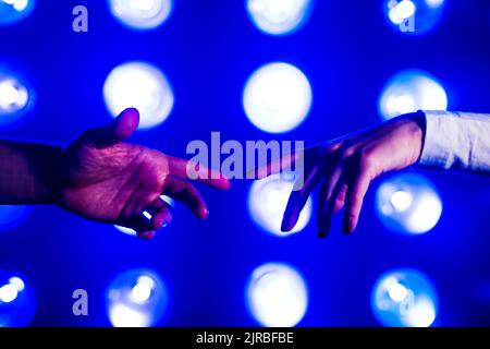 Hands of couple reaching towards each other in front of illuminated lights Stock Photo