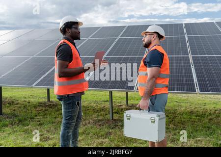 Engineer holding tablet PC discussing with coworker at solar station Stock Photo