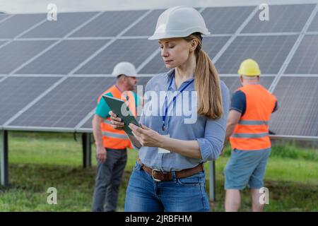 Woman using tablet PC with colleagues in background at solar station Stock Photo