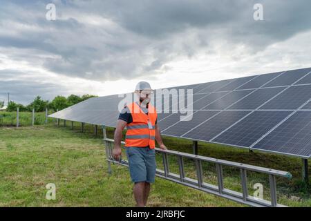 Engineer with ladder walking by solar panels Stock Photo
