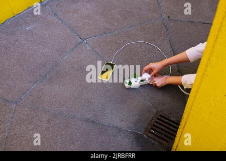 Hands of young woman charging cell phone with electrical outlet and plants on floor Stock Photo