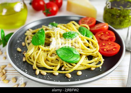 Traditional italian pasta with fresh vegetables, parmesan cheese, basil leaves, pine nuts and pesto sauce in black plate on white wooden background. Stock Photo