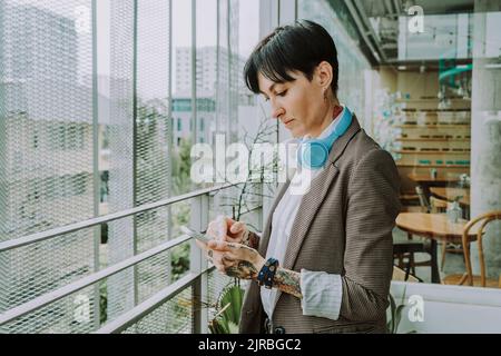 Businesswoman with short hair surfing net through smart phone in cafe Stock Photo