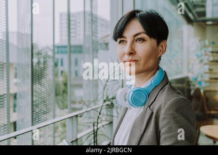 Thoughtful businesswoman wearing wireless headphones sitting in office ...