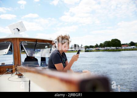 Boy using smart phone sitting on boat deck Stock Photo