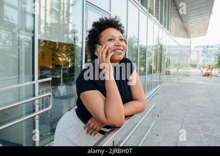 Smiling businesswoman talking on mobile phone leaning on railing Stock Photo