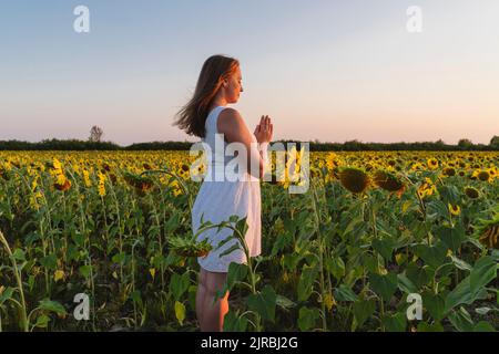 Woman with hands clasped meditating at sunflower field on sunset Stock Photo