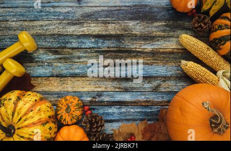 Dumbbells, various pumpkins, squashes and gourds. Gym fitness flat lay autumn composition, with cones, corn, fall leaves. Copy space on wooden bg. Stock Photo