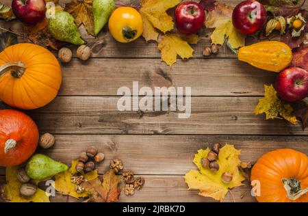 Autumn flat lay composition frame with pumpkins, walnuts, hazelnuts, apples, kaki persimmon, pears and fall leaves. Copy space on wooden background. Stock Photo
