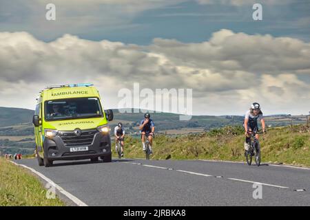 7thAug22 Gower Swansea Wales UK Triathlon Ironman cycling event Ground level shot. Ambulance with blue lights overtaking cyclists enroute to incident Stock Photo