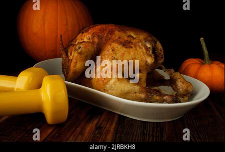 Roasted homemade chicken for Thanksgiving dinner, with pumpkins and two gym dumbbells. Autumn composition, healthy fitness lifestyle, diet concept. Stock Photo