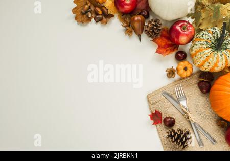 Pumpkins, apples, cones, leaves, acorns, chestnuts, with fork and knife on a jute material for Thanksgiving dinner or Halloween. Stock Photo