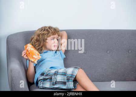 Happy handsome young teen boy holding slice pizza. Child delicious Italian pizzas. Happy child biting off big slice fresh made pizza. Little boy Stock Photo