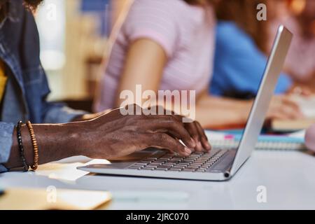Close up of black young man typing on laptop keyboard while studying in college library with students in row, copy space Stock Photo
