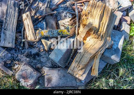 Close-up of an unlit campfire against gray and black extinguished ashes, stones surrounding wooden logs from tree trunks found in forest, moss, arrang Stock Photo