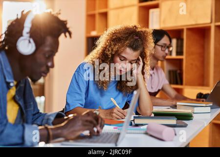 Diverse group of students in row studying in college library, focus on young woman writing in notebook Stock Photo