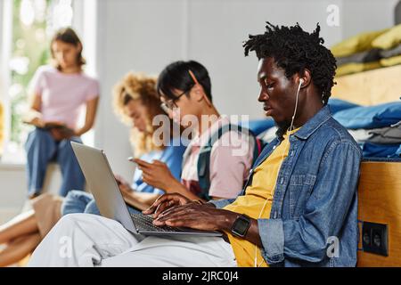 Diverse group of students in row studying, focus on African American young using laptop in foreground Stock Photo