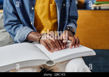 Close up of blind African American man reading book in braille in college library lounge Stock Photo