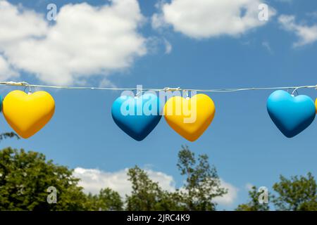 Garland in the form of yellow and blue hearts against the blue sky. The concept of support for Ukraine. Stock Photo