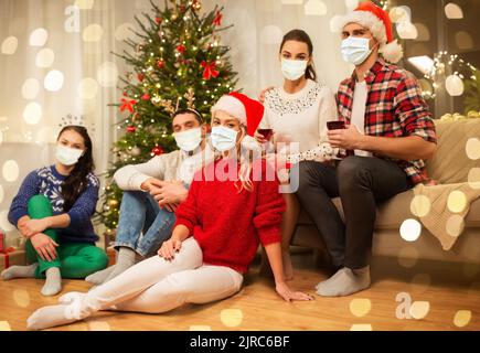 friends in masks drinking wine on christmas Stock Photo