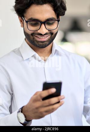 Happy young indian business man using smartphone at work in office. Vertical Stock Photo