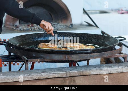 Cook roasts flour pastries in a large pan with butter outdoor Stock Photo