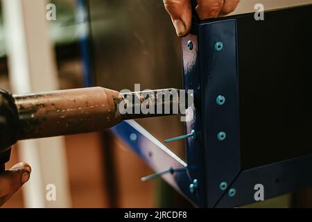 Male worker uses electric riveting gun. Hand holding  riveting machine and placing rivets. Working workshop of carpenter or mechanic. Stock Photo