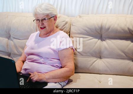 happy elderly woman using laptop computer at home. Senior mature older woman watching business training, online webinar on laptop computer remote work Stock Photo
