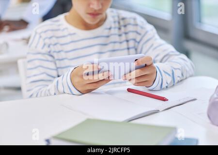 Minimal close up of child holding smartphone and playing mobile game in school Stock Photo
