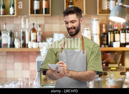 smiling waiter in apron taking notes to notepad Stock Photo