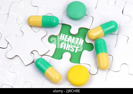 Medicine concept. There are pills and vitamins on the white puzzles. Inside on a green background the inscription - HEALTH FIRST Stock Photo