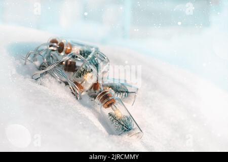 Christmas tree garland in the form of glass flasks with Christmas trees inside, lying on a light background of real snow. copy space Stock Photo