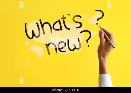 Man with pen writing text WHAT'S NEW? on yellow background Stock Photo